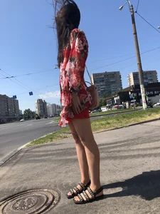 Hot street candid girl wearing a short dress and sandals standing on the crosswalk, wind is playing with her hair