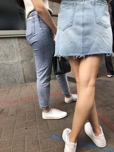 Hot slim legs closeups, street girl wearing a denim fringed skirt