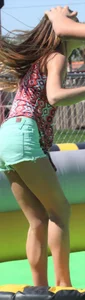 Brunette skinny teen in green shorts playing in a bounce house