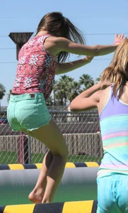 Brunette skinny teen in green shorts playing in a bounce house