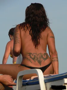 Topless tattooed lady on the beach with fake big tits
