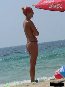 Topless skinny blonde lady in a g-string bikini at the beach