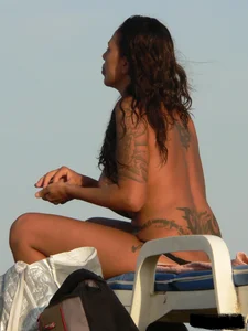 Topless tattooed lady on the beach with fake big tits