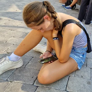 Cute skinny candid teen in denim shorts sitting on the pavement on the street
