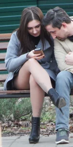 Nice candid girl with crossed legs in pantyhose sitting on a park bench reading something on her phone