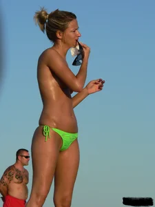 Topless girl on the beach with small boobs wearing a green thong bikini