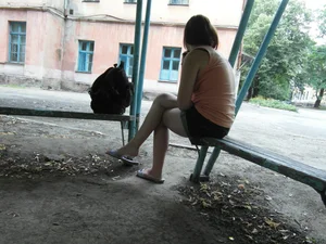 Young Candid Girl in Shorts Slippers Sitting Lonely on a Street Bench