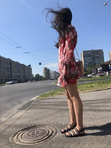 Hot street candid girl wearing a short dress and sandals standing on the crosswalk, wind is playing with her hair