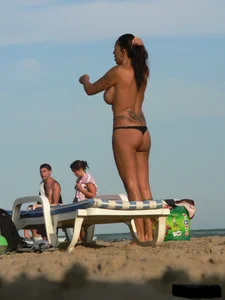 Topless tattooed lady on the beach with fake big tits