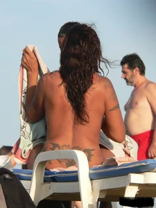 Topless tattooed lady on the beach with fake big tits