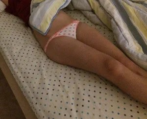 Girl Lying in Bed in Polka-Dot Panties With Her Belly Showing From Under Blanket