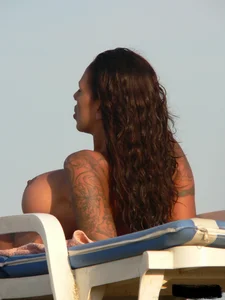 Topless tattooed lady on the beach with fake big tits