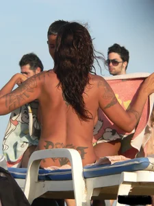 Topless tattooed lady on the beach with fake big tits