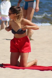 Hottie undressing from her red shorts to her bikini to layout on the beach