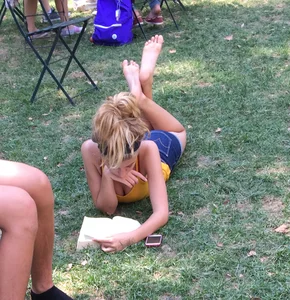 Girl in Denim Shorts Lying on the Grass Reading a Book with Her Bare Feet Raised Up Candid Photo