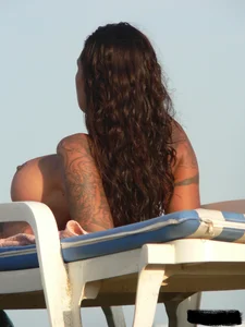 Topless tattooed lady on the beach with fake big tits