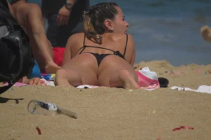 Bikini babe with a nice ass laying on the beach in a black bikini