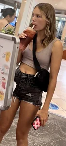 Candid girl in a top and denim fringed shorts drinking soda on the street