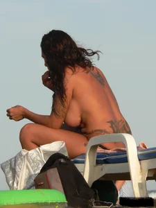 Topless tattooed lady on the beach with fake big tits