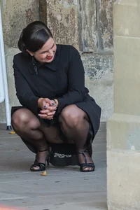 Candid girl wearing black pantyhose, a skirt and high heels squatting on the street flashing her panties