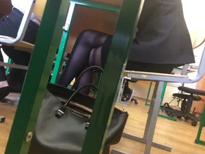 Crossed legs of a candid teen college girl sitting with crossed legs at the desk in classroom, wearing a short skirt and black pantyhose
