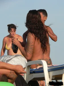 Topless tattooed lady on the beach with fake big tits
