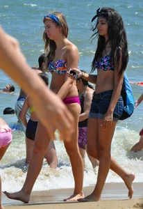Hot beach brunette in shorts and bikini top with her friend in bikini