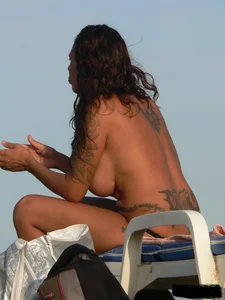 Topless tattooed lady on the beach with fake big tits