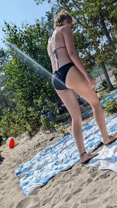 A pretty brown haired woman bending over with her nice ass in a black bikini on the beach. oc