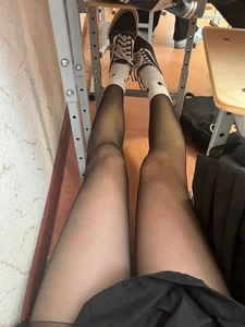 College girl's skinny legs in black pantyhose closeup in classroom under desk, white socks