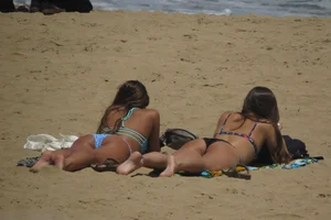 Two babes laying on the beach in bikinis with nice asses