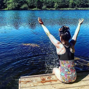 Girl in a one-piece swimsuit sitting on a pier by the lake and splashing