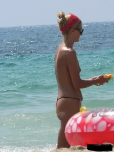 Topless skinny blonde lady in a g-string bikini at the beach