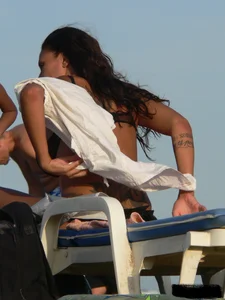 Topless tattooed lady on the beach with fake big tits