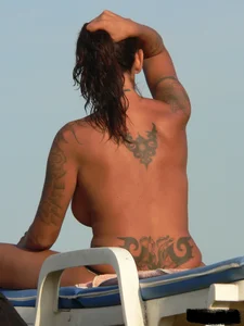 Topless tattooed lady on the beach with fake big tits