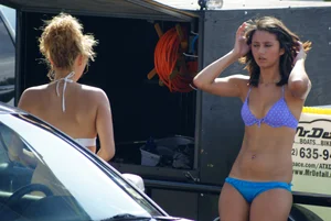 Beautiful skinny brunette at a car wash in blue and purple bikini