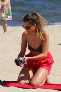 Hottie undressing from her red shorts to her bikini to layout on the beach