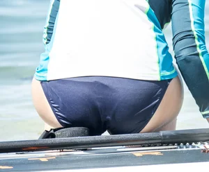 Girl in the water in a navy blue bikini bottom, shirt and hat with a nice ass