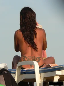Topless tattooed lady on the beach with fake big tits
