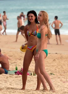 Sexy brunette in thong bikini and blonde friend in green bikini at the beach
