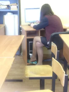 Teen in a skirt and pantyhose sitting in college class, dangling her shoes