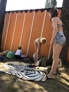 Young Skinny Girl Taking Off Her Denim Shorts Leaving a Swimsuit - Bending Over While Laying a Blanket on the Ground at a Lake Nature Park Gallery