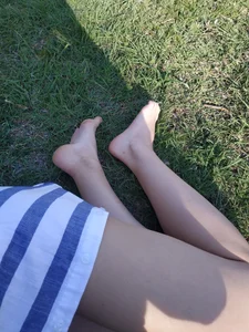 Candid girl with hot legs chilling on the grass in a park and showing off her feet