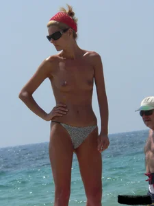 Topless skinny blonde lady in a g-string bikini at the beach