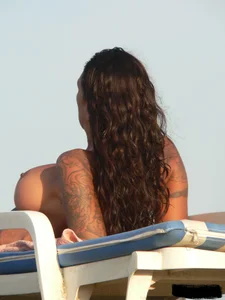 Topless tattooed lady on the beach with fake big tits