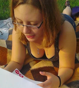 Bespectacled teen lying on her stomach on the grass while reading