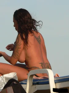 Topless tattooed lady on the beach with fake big tits