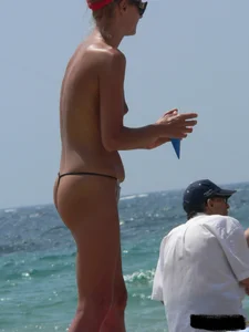 Topless skinny blonde lady in a g-string bikini at the beach