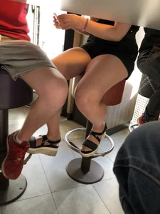 Legs in Shorts and Sandals Under Table in the Cafe Creepshot