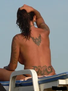 Topless tattooed lady on the beach with fake big tits